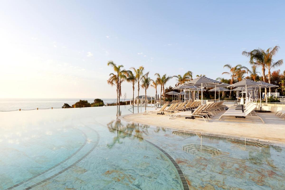 una piscina con sillas y sombrillas junto a la playa en BLESS Hotel Ibiza - The Leading Hotels of The World, en Es Canar