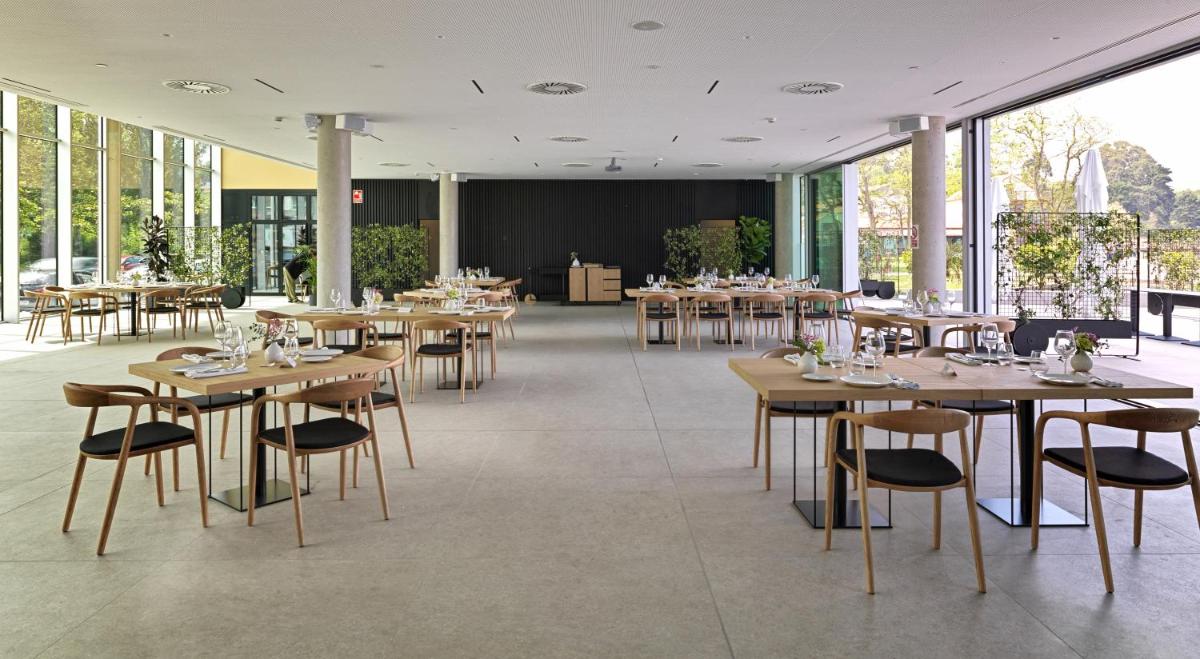 Un restaurante con mesas y sillas de madera y ventanas. en Noa Boutique Hotel, en Santa Cruz de Oleiros
