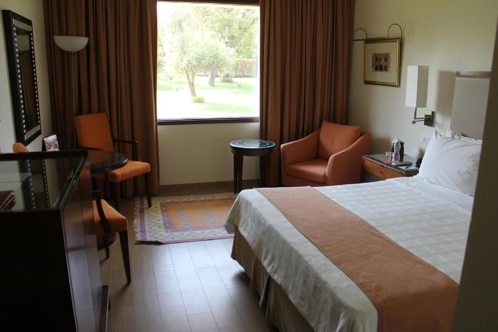 a hotel room with a bed and a chair and a window at Trident Agra in Agra