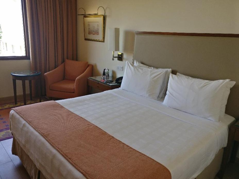 a hotel room with a large bed and a chair at Trident Agra in Agra