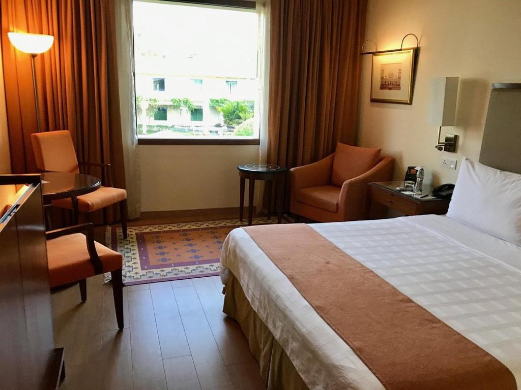 a hotel room with a bed and a desk and a window at Trident Agra in Agra