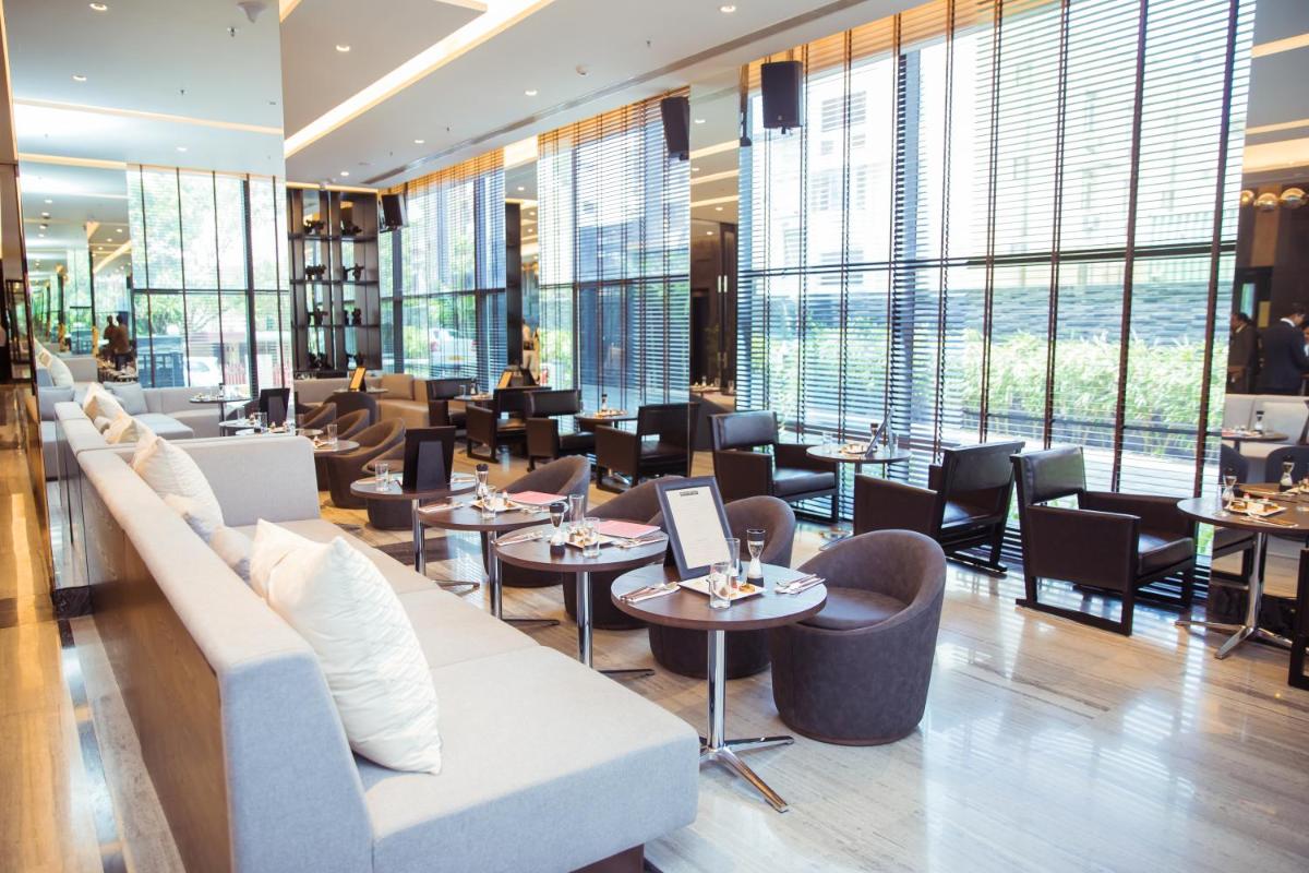 a restaurant with couches and tables and windows at Novotel Chennai Chamiers Road in Chennai