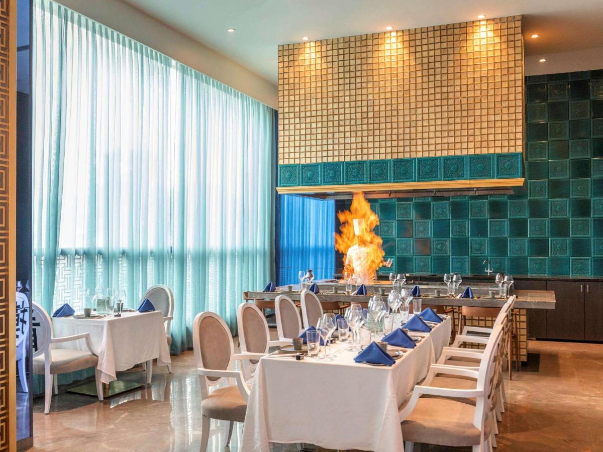 a dining room with white tables and chairs and a fireplace at Novotel Vijayawada Varun in Vijayawāda