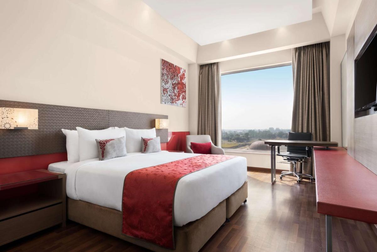 a hotel room with a bed and a desk and a window at Ramada by Wyndham Lucknow Hotel and Convention Center in Lucknow
