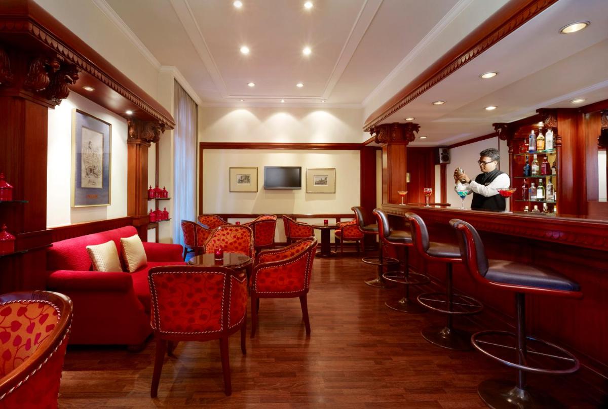 a bar with red chairs and a man standing behind the bar at Taj Ganges Varanasi in Varanasi