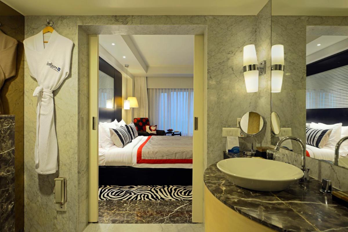 a bathroom with a sink and a bedroom with a bed at Radisson Blu Hotel Ahmedabad in Ahmedabad