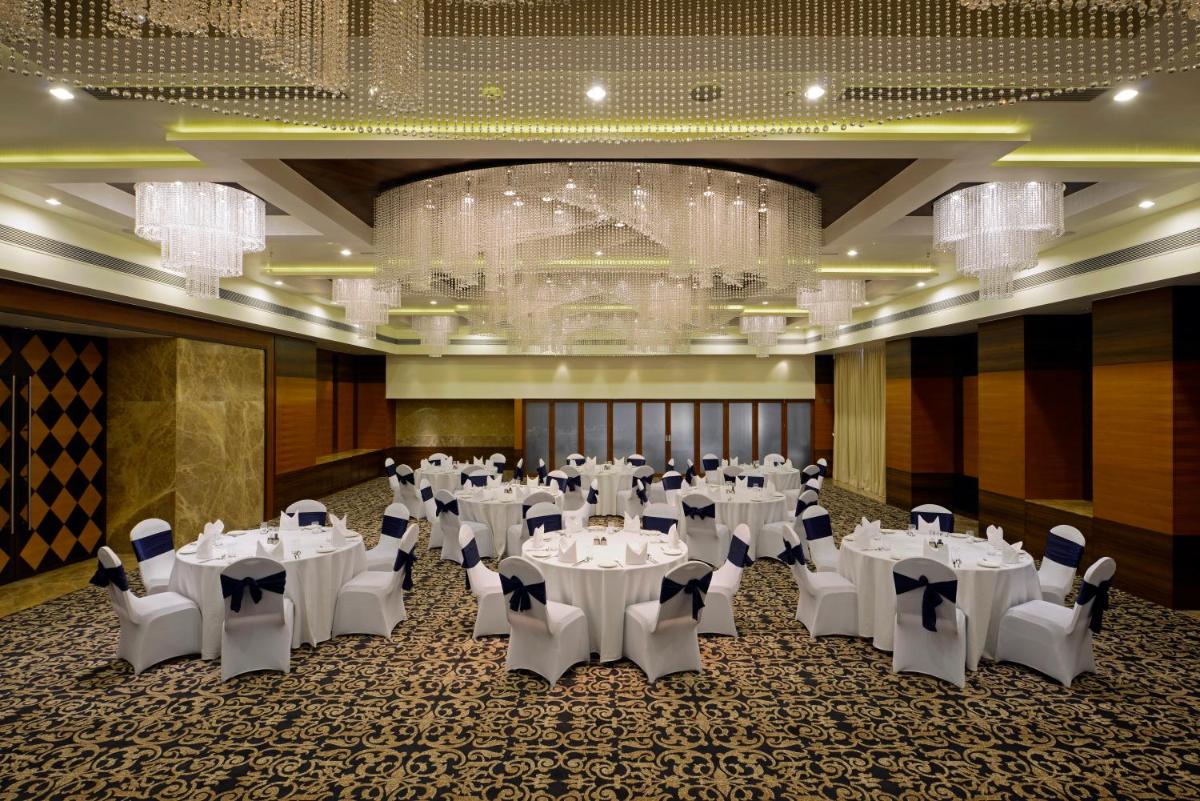 a banquet hall with white tables and chairs and a chandelier at Radisson Blu Hotel Ahmedabad in Ahmedabad