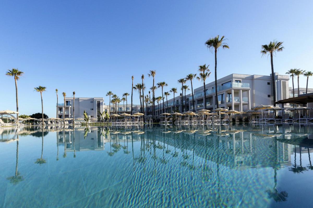 Una gran piscina de agua con palmeras y edificios. en Hipotels Barrosa Park, en Chiclana de la Frontera