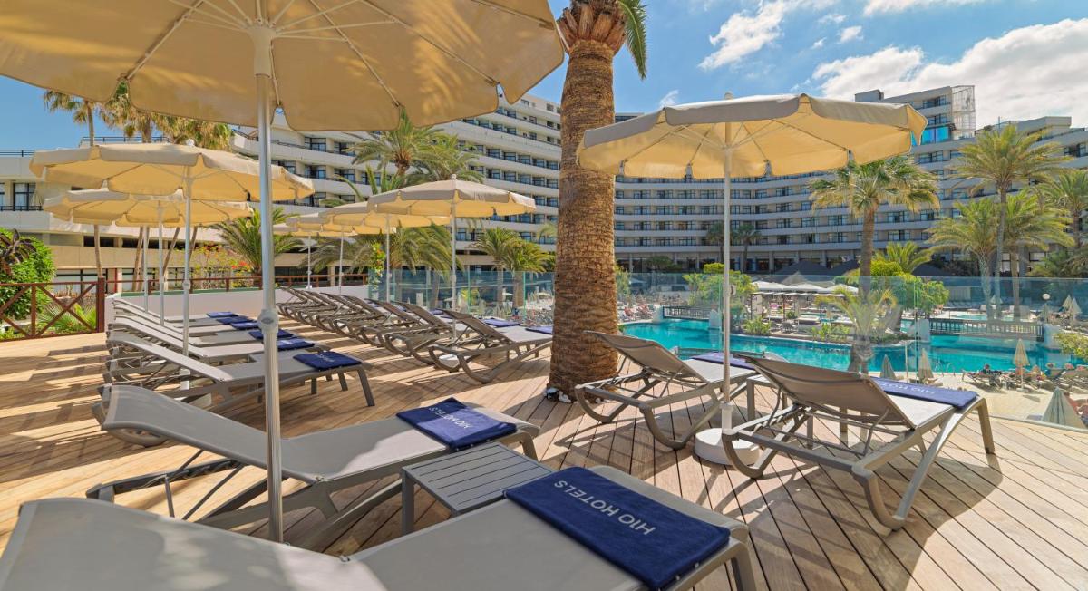 Un grupo de sillas y sombrillas junto a una piscina. en H10 Conquistador, en Playa de las Américas