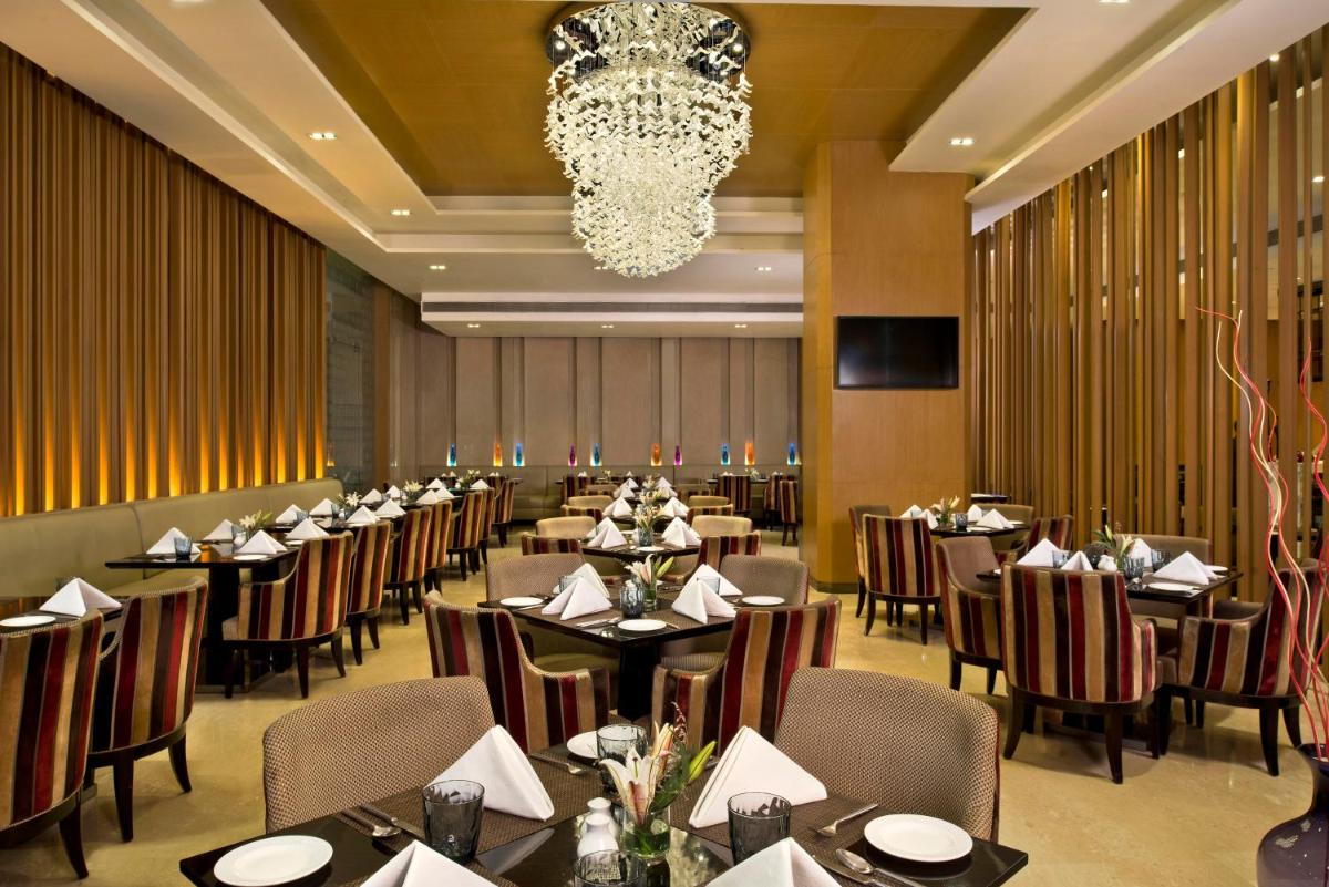 a dining room with tables and chairs and a chandelier at Radisson Blu Jaipur in Jaipur