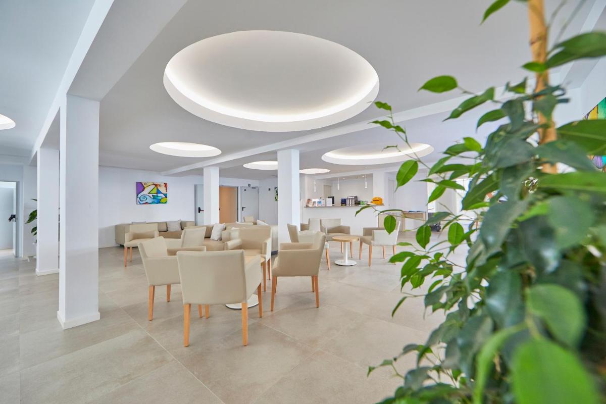 Una sala de espera con sillas y mesas en un edificio. en Hotel Ilusion Moreyo - Adults Only, en Cala Bona