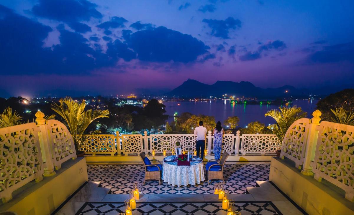 a man standing on a balcony at night with a table at The Lalit Laxmi Vilas Palace in Udaipur