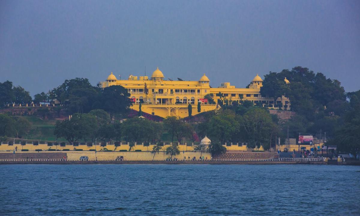 a large yellow building on a hill next to a body of water at The Lalit Laxmi Vilas Palace in Udaipur