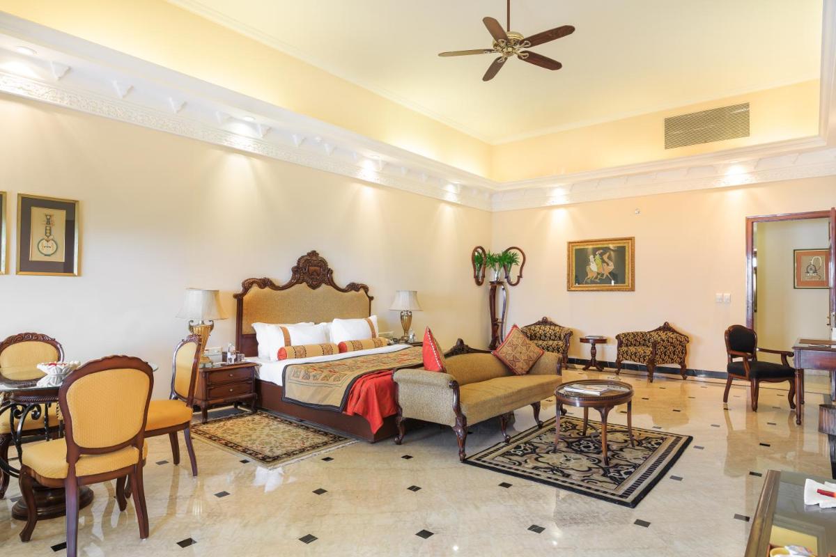 a bedroom with a bed and a couch and chairs at The Lalit Laxmi Vilas Palace in Udaipur