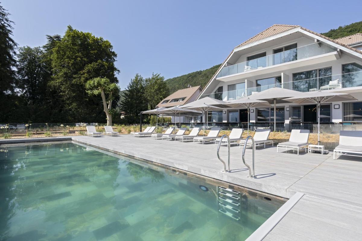 une piscine avec des chaises longues et des parasols devant un bâtiment dans l'établissement Black Bass Hotel, à Sévrier