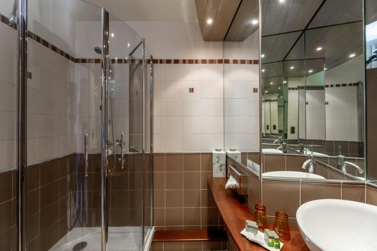 une salle de bain avec deux lavabos et une douche en verre dans l'établissement Le Bailliage Hôtel & Spa, à Salers