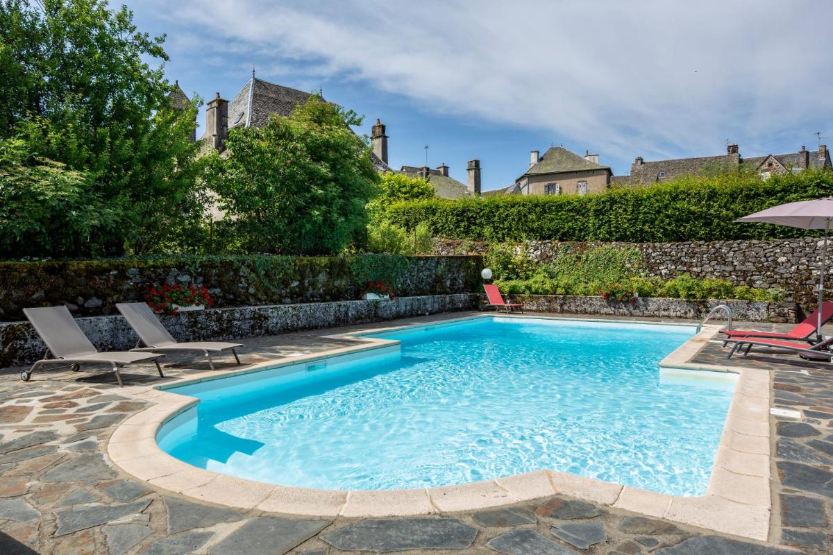 une piscine avec deux chaises et un parasol dans l'établissement Le Bailliage Hôtel & Spa, à Salers