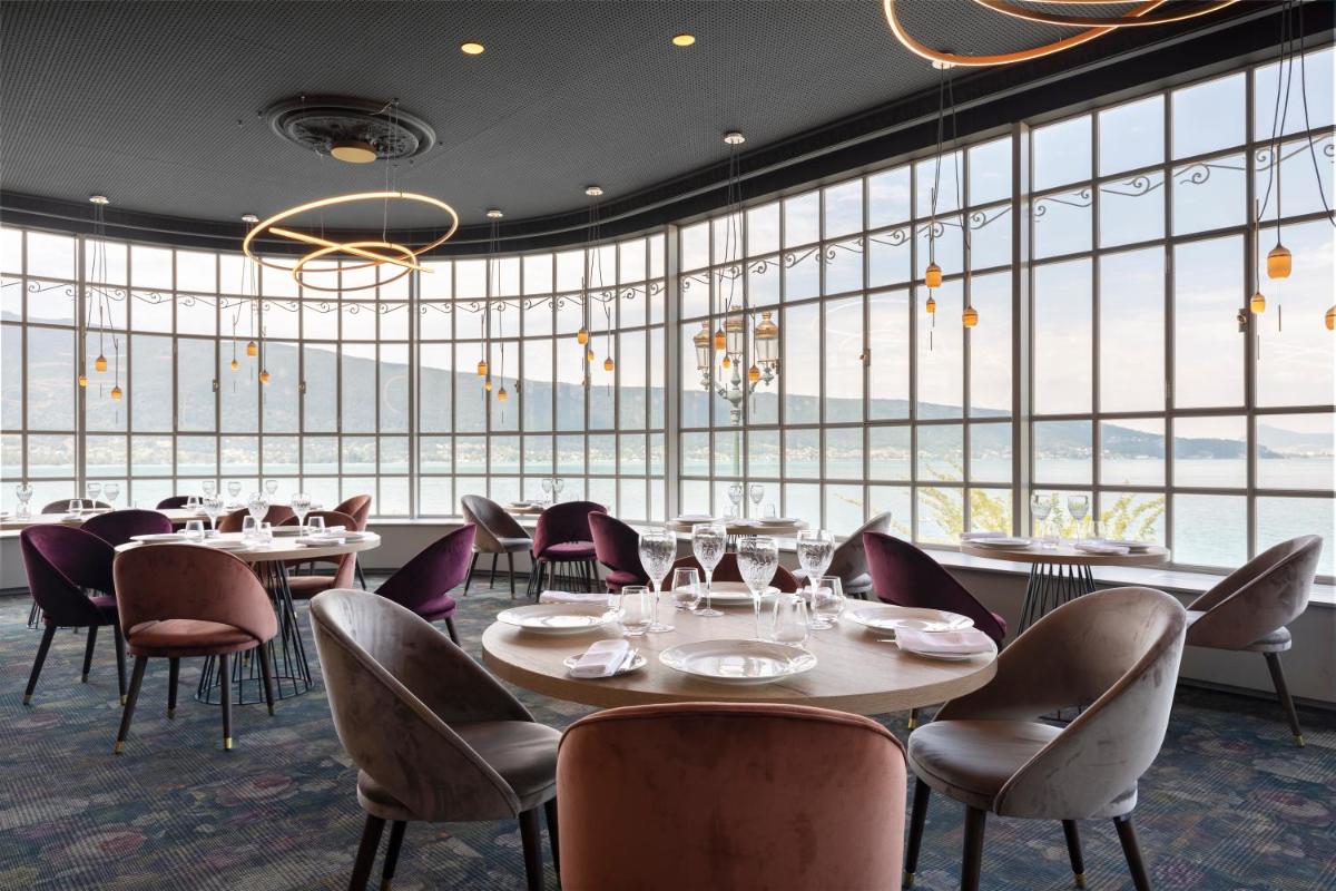 un restaurant avec des tables et des chaises et de grandes fenêtres dans l'établissement Le Palace De Menthon, à Menthon-Saint-Bernard