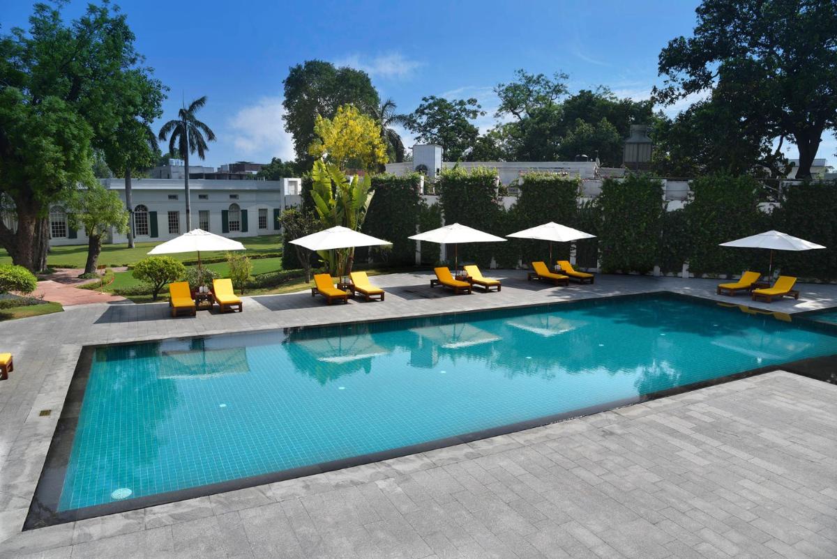 a swimming pool with chairs and umbrellas at Maidens Hotel New Delhi in New Delhi