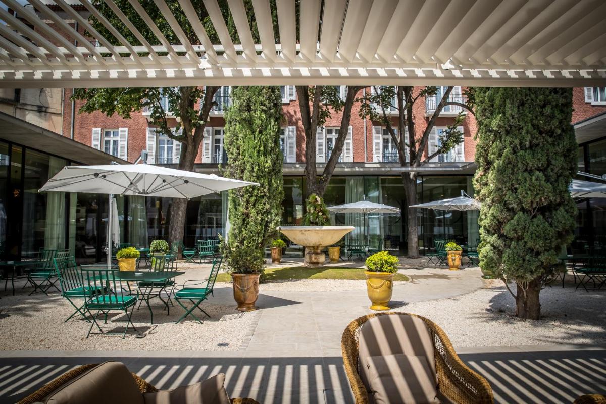 une terrasse avec des chaises, des tables et un parasol dans l'établissement Maison Albar Hotels L’Imperator, à Nîmes