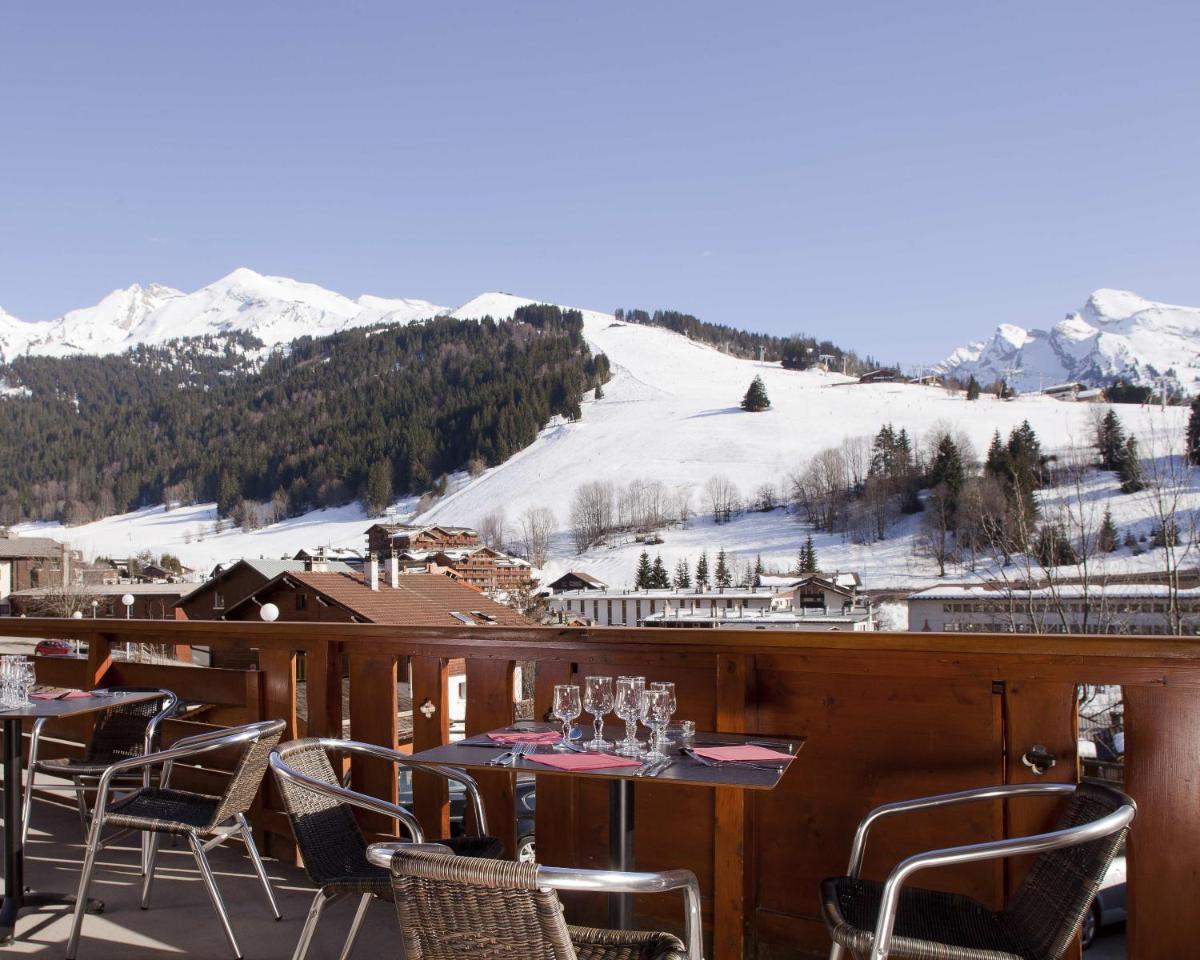 d'un balcon avec des tables, des chaises et une montagne enneigée. dans l'établissement Beaulieu, à La Clusaz