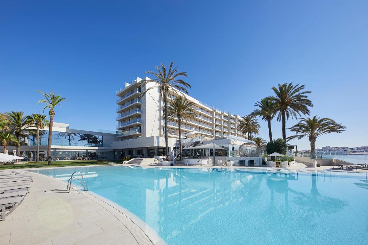 Una gran piscina con palmeras y un edificio. en Hotel Torre del Mar - Ibiza, en Playa d'en Bossa