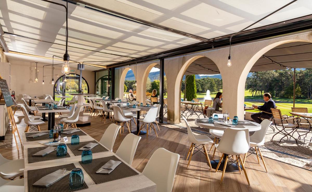 un restaurant avec des tables et des chaises et des personnes en arrière-plan dans l'établissement Château et Golf De Taulane, à La Martre