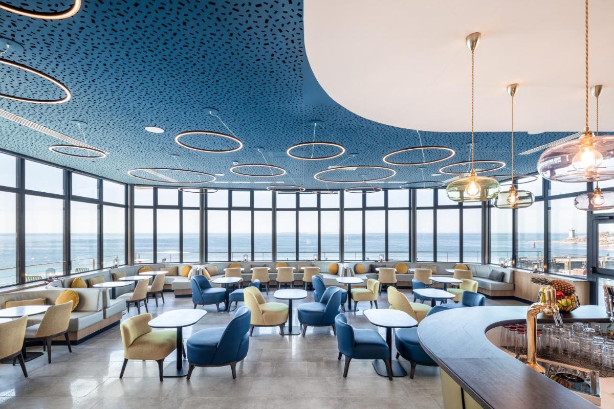 un restaurant avec des chaises, des tables et des fenêtres bleues dans l'établissement Sainte-Barbe Hotel & Spa Le Conquet - MGallery Collection, au Conquet