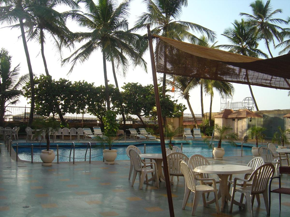 a pool with tables and chairs and palm trees at Ramada Plaza By Wyndham Palm Grove in Mumbai