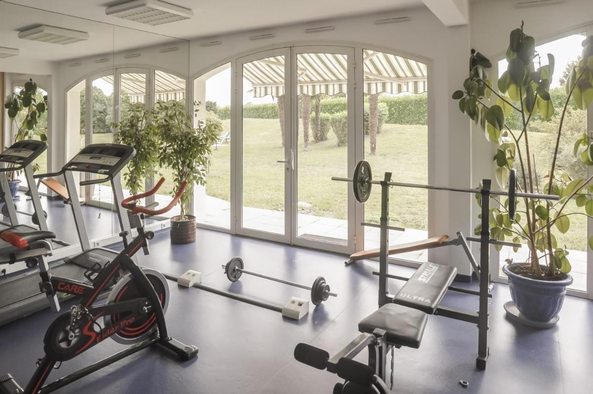 - une salle de sport avec plusieurs appareils d'exercice dans une pièce dotée de fenêtres dans l'établissement Alysson Hôtel, à Oloron-Sainte-Marie