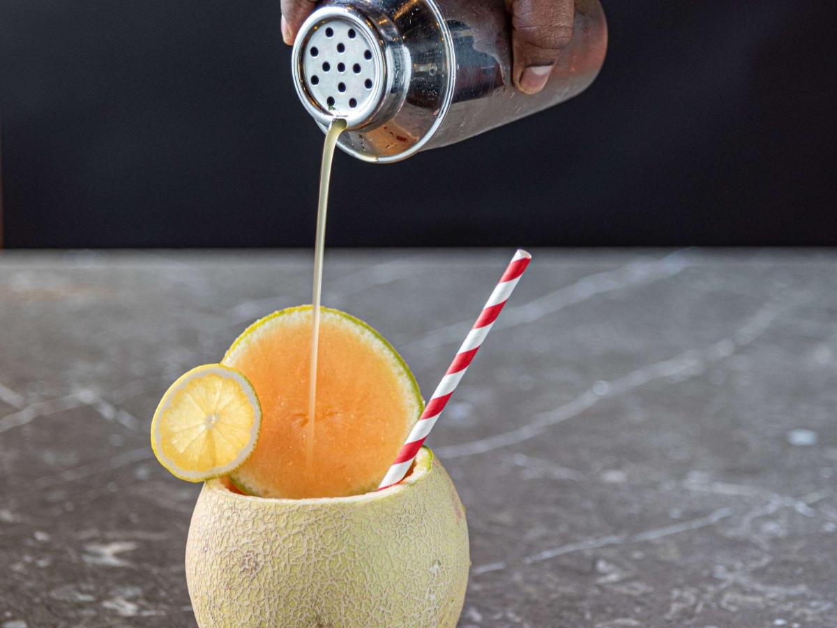 a person pouring a drink into a cup with an orange at Mercure Hyderabad KCP Banjara Hills, An Accor Hotel in Hyderabad