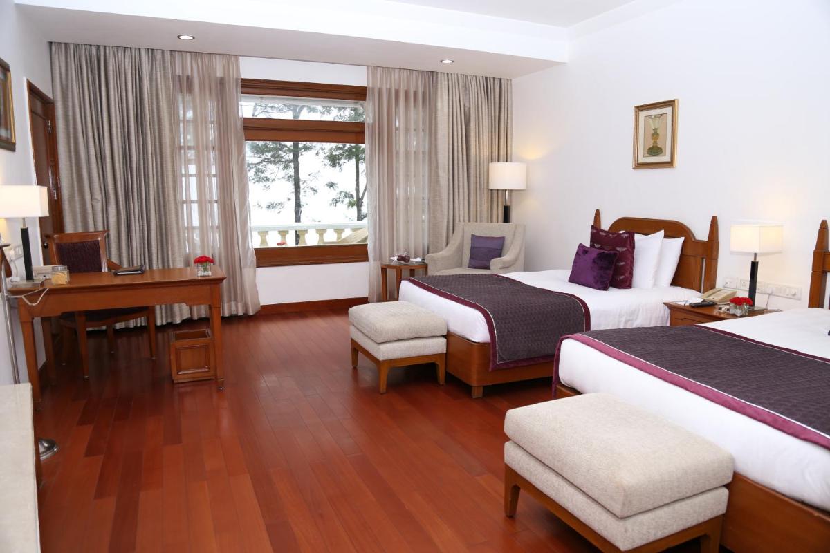 a hotel room with two beds and a desk at Jaypee Residency Manor in Mussoorie a hotel room with two beds and a desk at Jaypee Residency Manor in Mussoorie