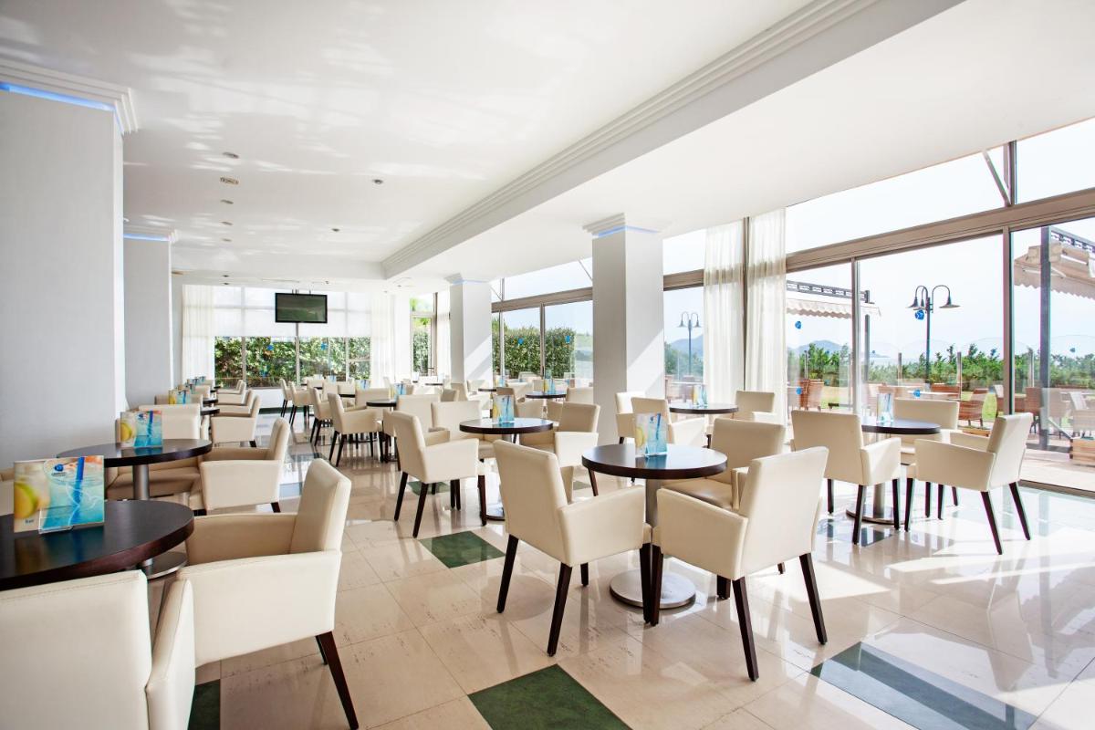 Un restaurante con mesas, sillas y ventanas. en Grupotel Natura Playa, en Playa de Muro