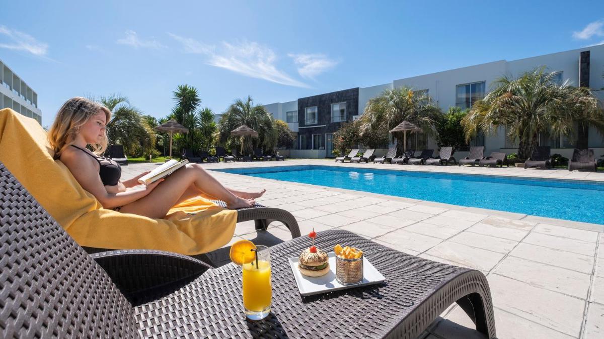 uma mulher sentada numa cadeira a ler um livro à beira da piscina em Hotel Vale Do Navio em Capelas