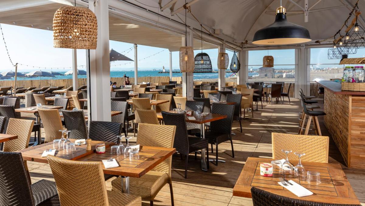 un restaurant avec des tables et des chaises et l'océan dans l'établissement Thalazur Port-Camargue - Hotel & Spa, au Grau-du-Roi