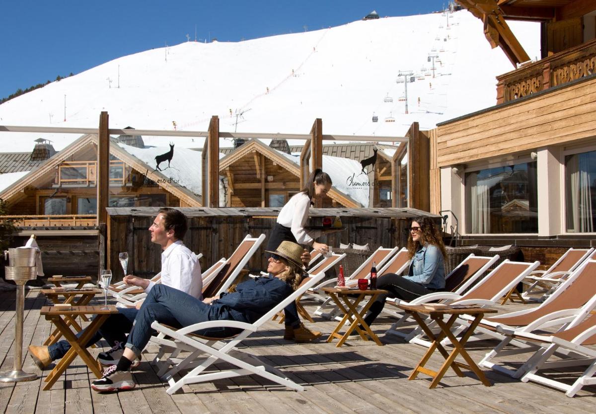 un groupe de personnes assises sur des chaises longues sur une terrasse dans l'établissement Hôtel Au Chamois d'Or by Les Etincelles, à L'Alpe-d'Huez