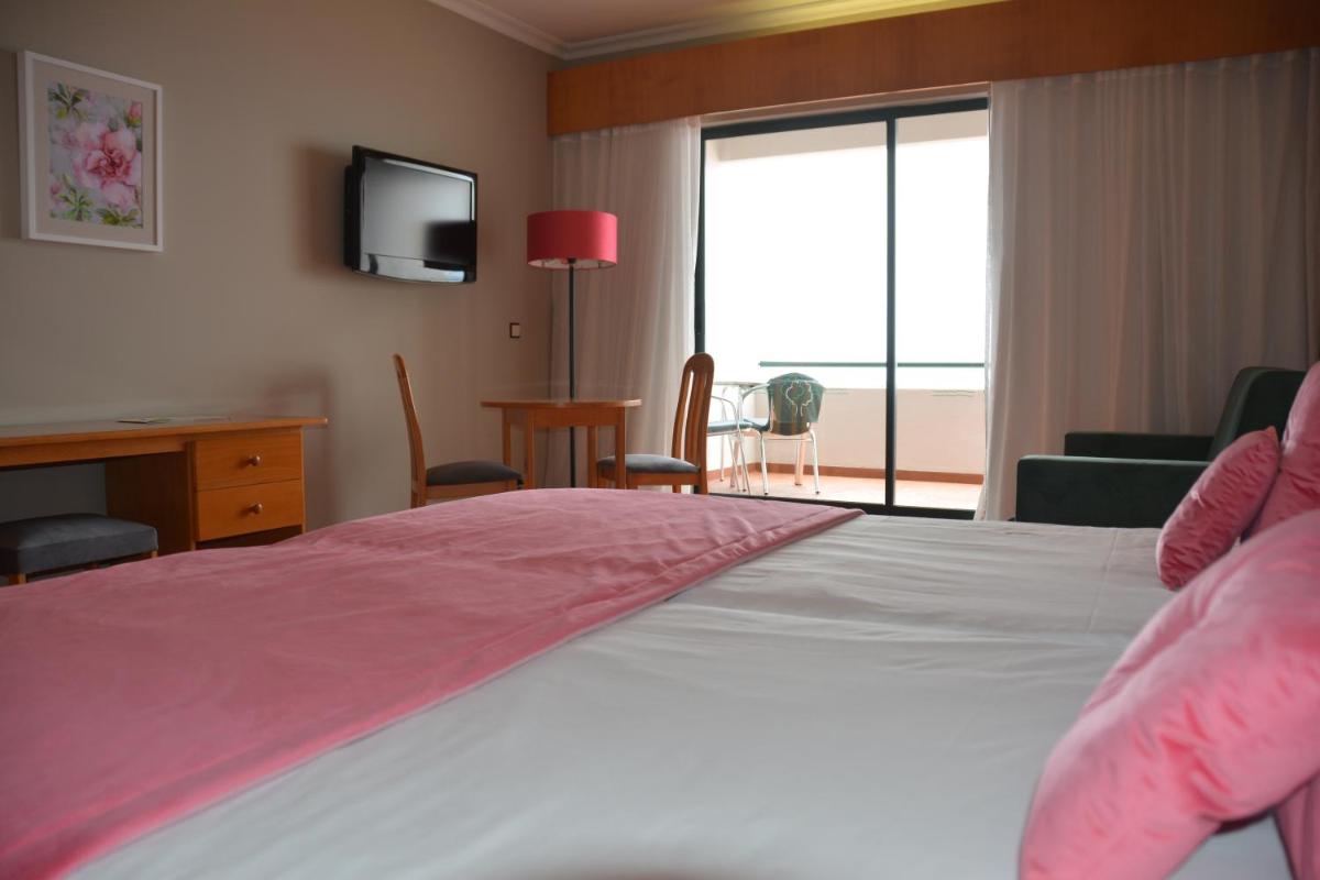 um quarto com uma cama com lençóis cor-de-rosa e uma televisão em Hotel Jardim Atlantico na Calheta mais 35 fotografias