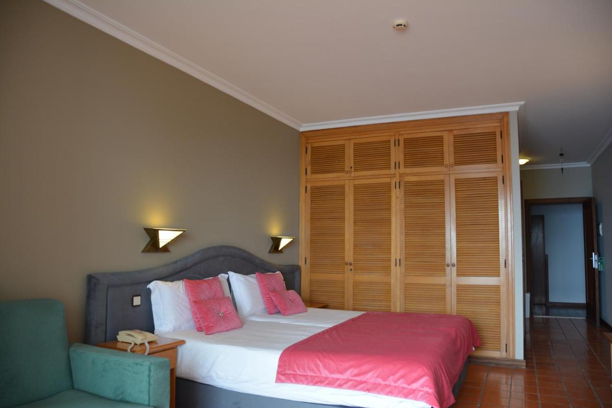 um quarto com uma cama com almofadas rosa e brancas em Hotel Jardim Atlantico na Calheta