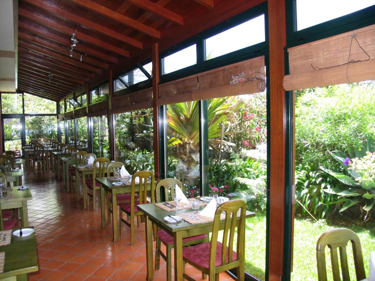 uma sala de jantar com mesas, cadeiras e janelas em Hotel Jardim Atlantico na Calheta