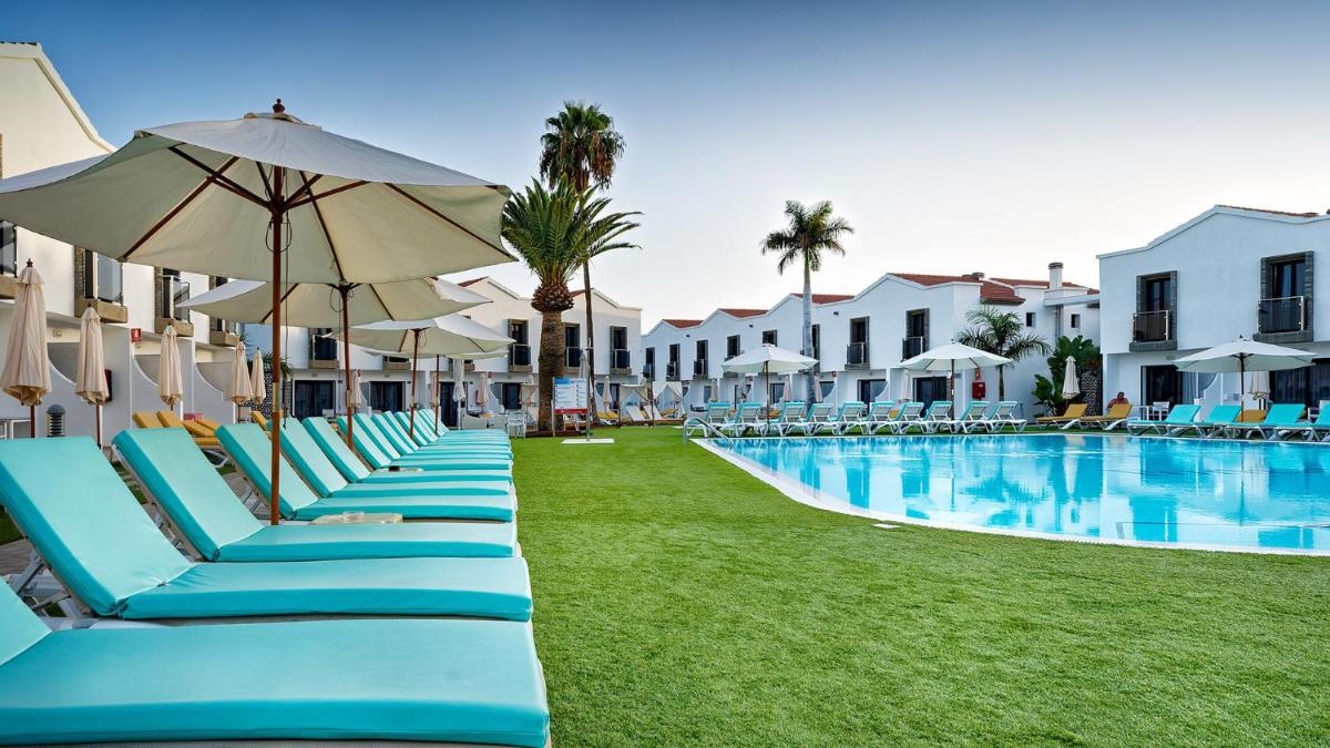 una fila de sillas y sombrillas azules junto a una piscina en FBC Fortuny Resort - Adults Only, en Maspalomas