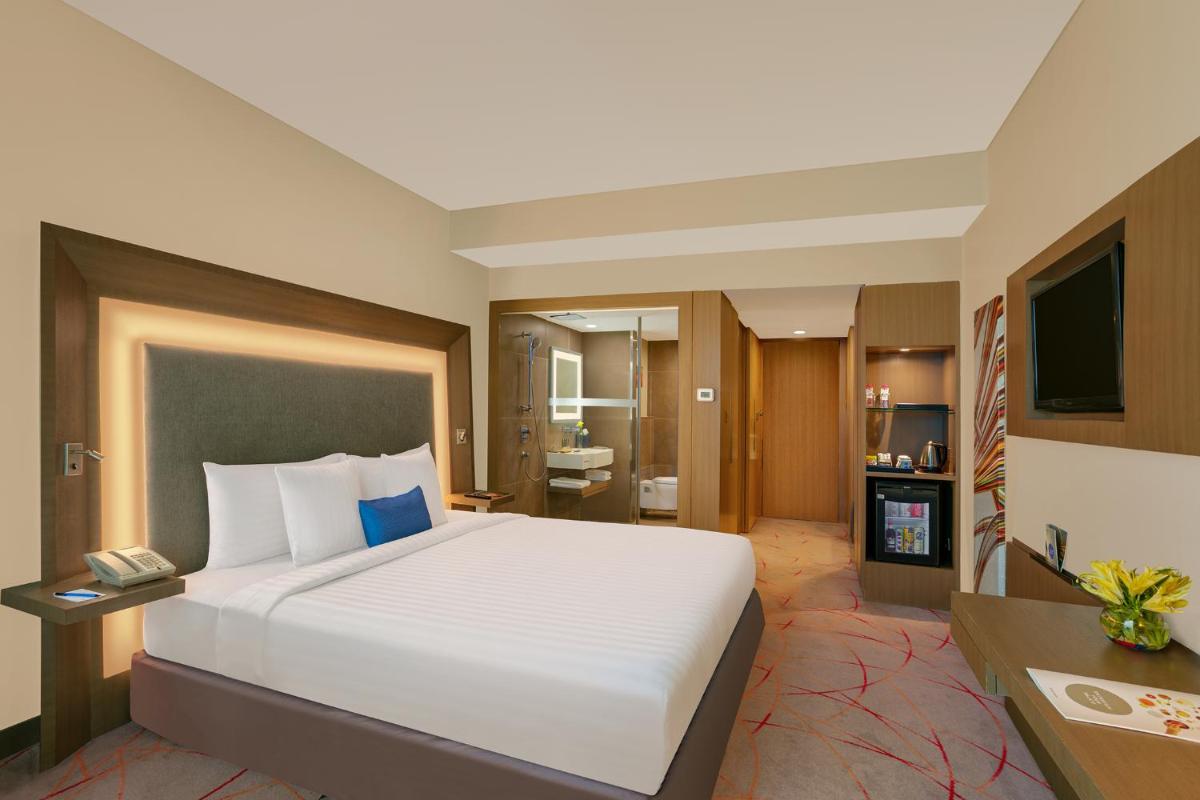 a hotel room with a large bed and a bathroom at Novotel Ahmedabad in Ahmedabad