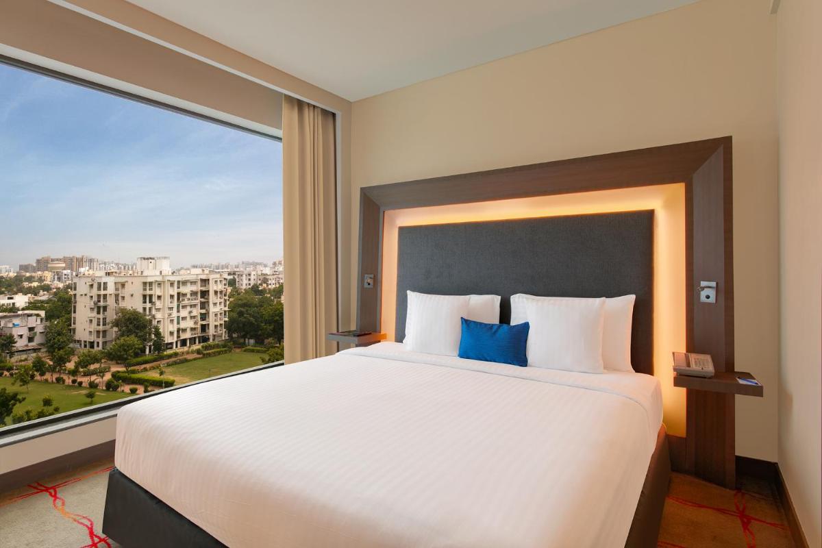 a bedroom with a large bed with a large window at Novotel Ahmedabad in Ahmedabad