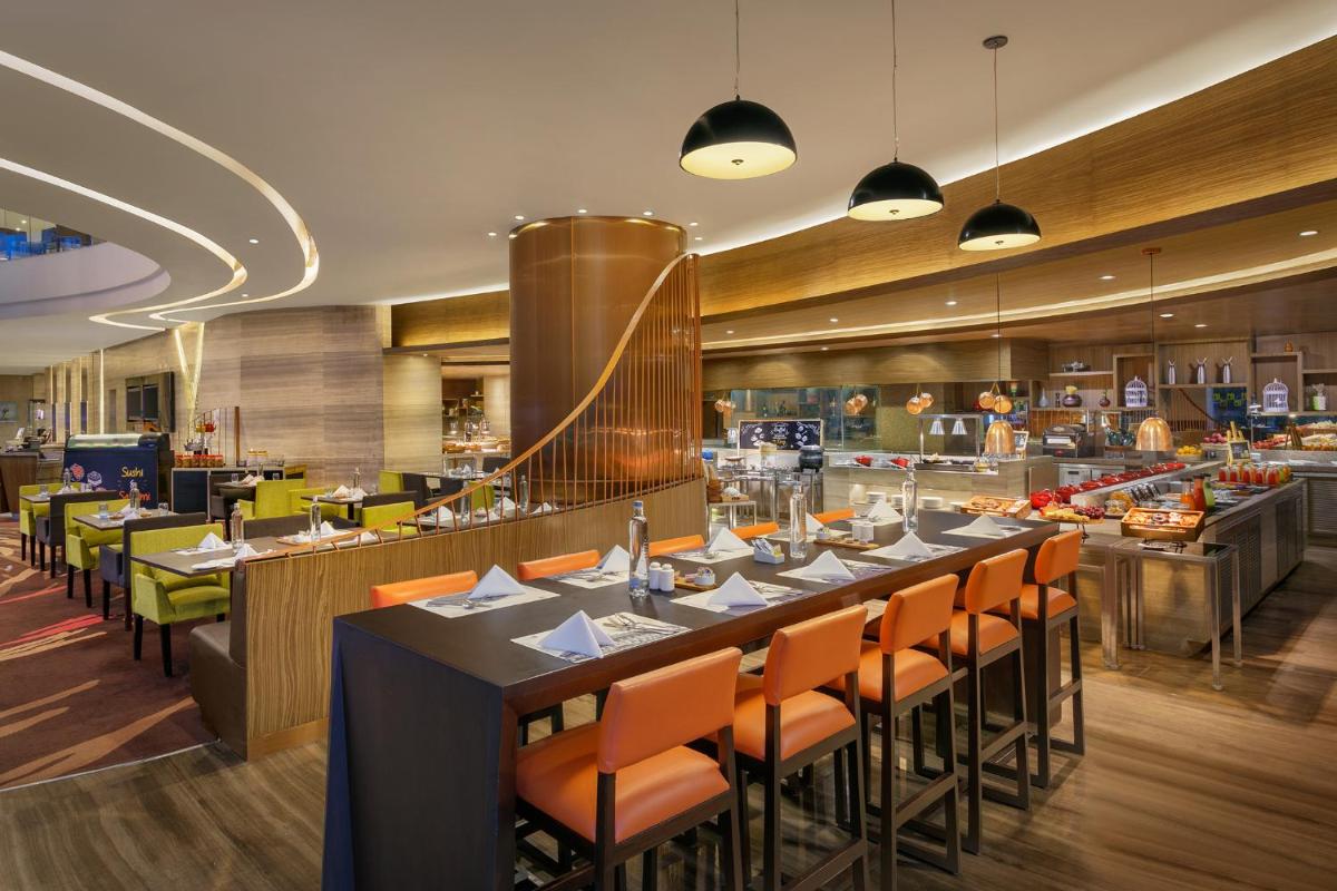 a restaurant with a long table with orange chairs at Novotel Ahmedabad in Ahmedabad