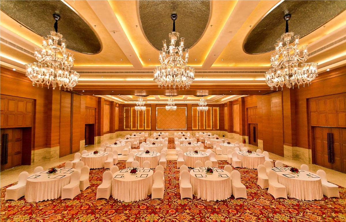 a large banquet hall with white tables and chandeliers at The Lalit Jaipur in Jaipur