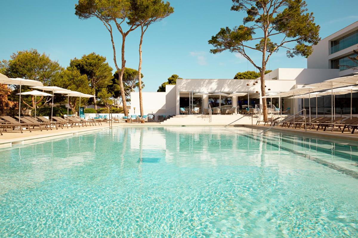 Una gran piscina con sillas y un edificio. en Diamant Hotel & Aparthotel, en Cala Ratjada