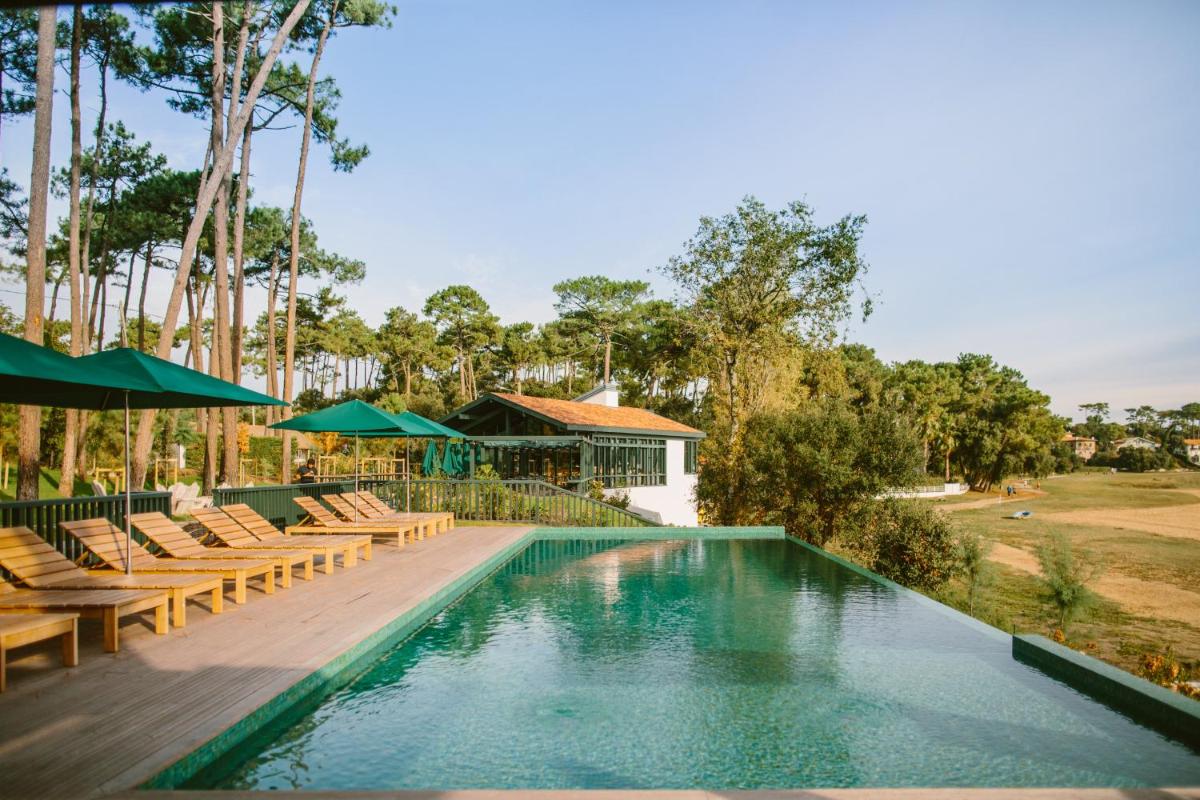 une piscine avec chaises longues et parasols dans un complexe hôtelier dans l'établissement Les Hortensias du Lac - Fontenille Collection, à Hossegor