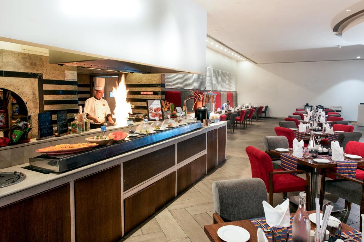 a chef preparing food in a restaurant with tables at Welcomhotel by ITC Hotels, Dwarka, New Delhi in New Delhi a chef preparing food in a restaurant with tables at Welcomhotel by ITC Hotels, Dwarka, New Delhi in New Delhi