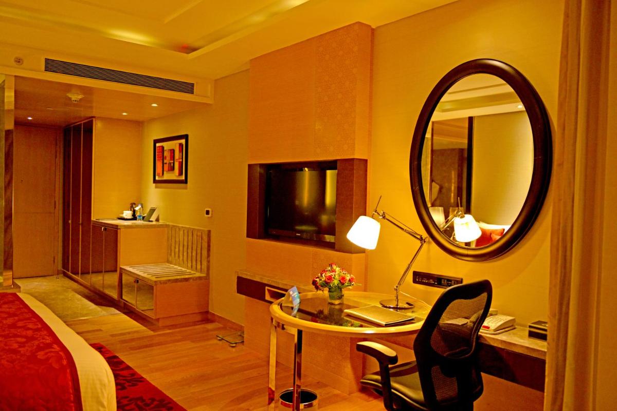 a bedroom with a bed and a desk with a mirror at Radisson Blu Jaipur in Jaipur