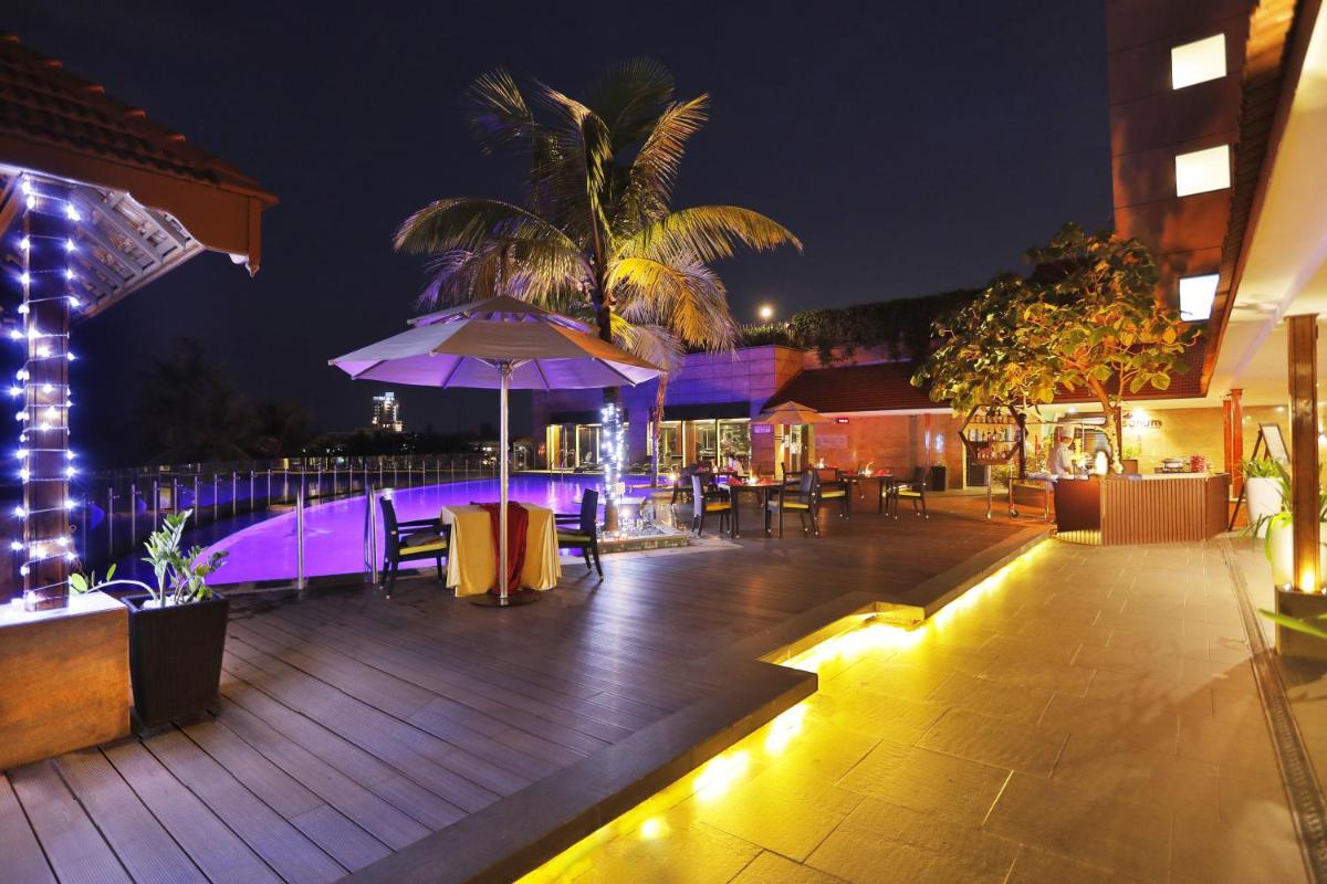 a patio with an umbrella and tables and chairs at night at Crowne Plaza Kochi by IHG in Cochin