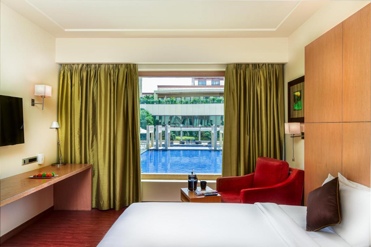 a hotel room with a bed and a red chair and a window at Novotel Hyderabad Airport in Hyderabad